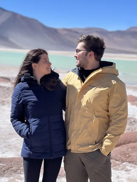 Helena e William sorrindo um para o outro diante de uma lagoa